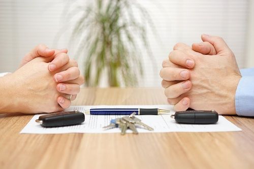 Two pairs of hands across a table, resting on a piece of paper with a pen, key fobs and keys.